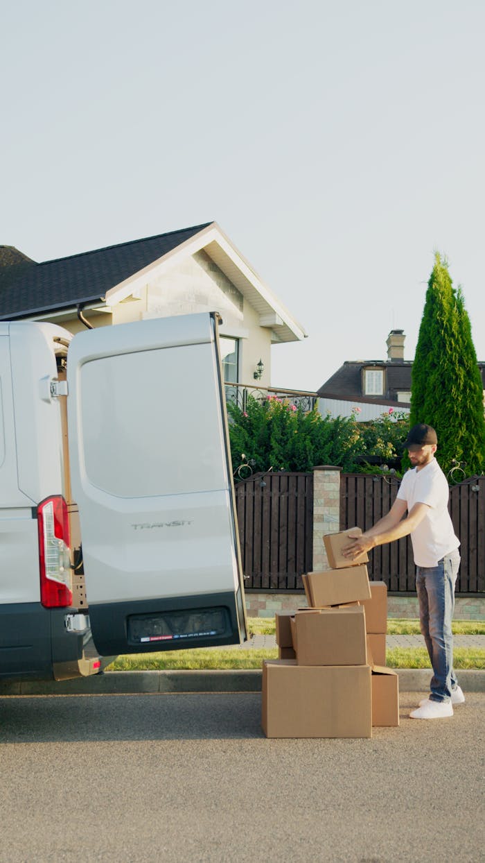 A delivery man organizing packages into a van outside a suburban house.